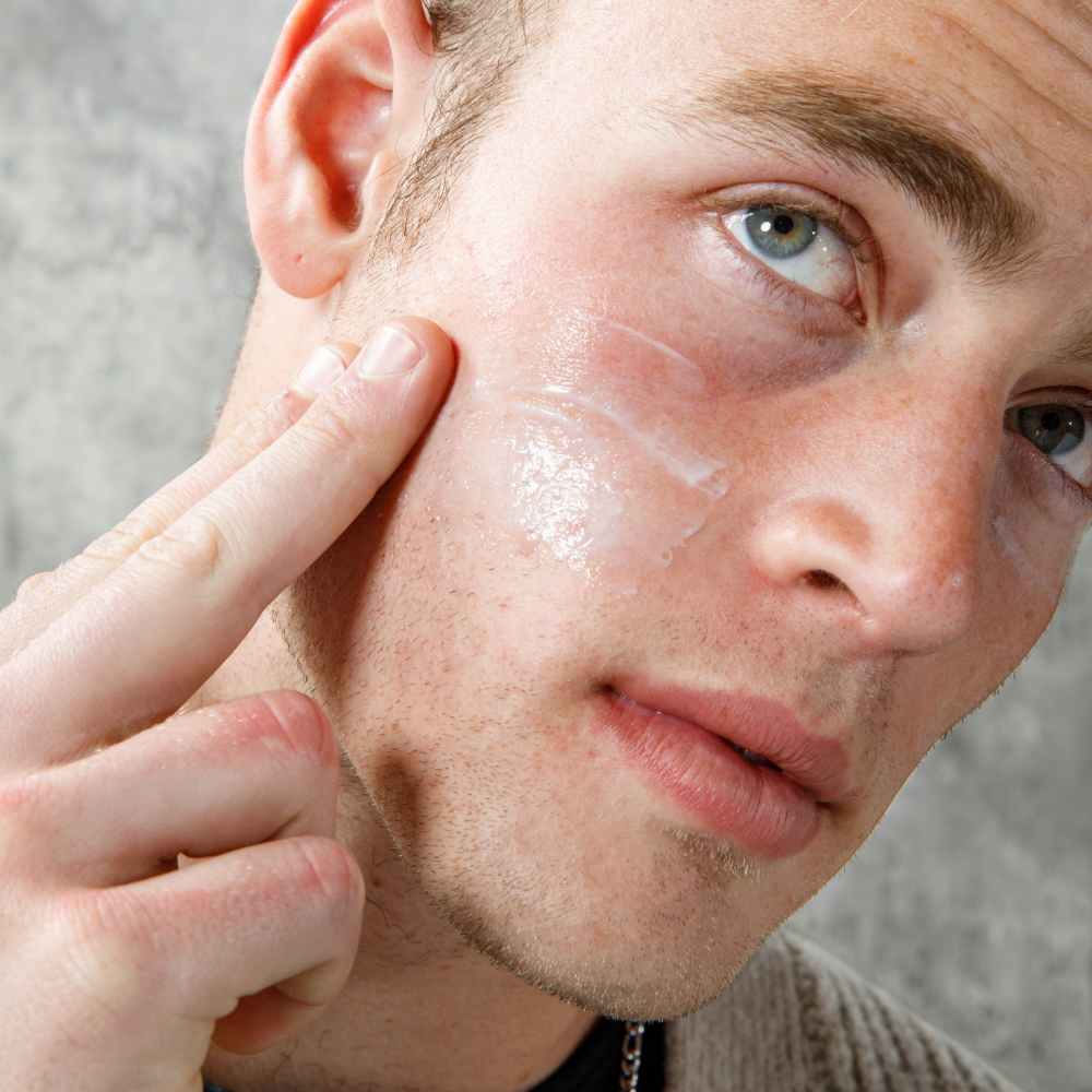 Man with blue eyes applying transparent moisturizing face cream on cheek, skincare routine for men, close-up