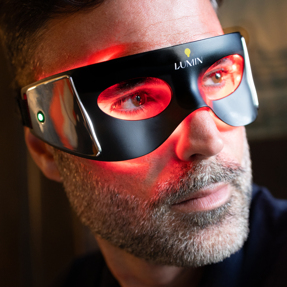 Man wearing black LUMIN LED light therapy glasses with red glow on face, promoting skin care and anti-aging treatment.