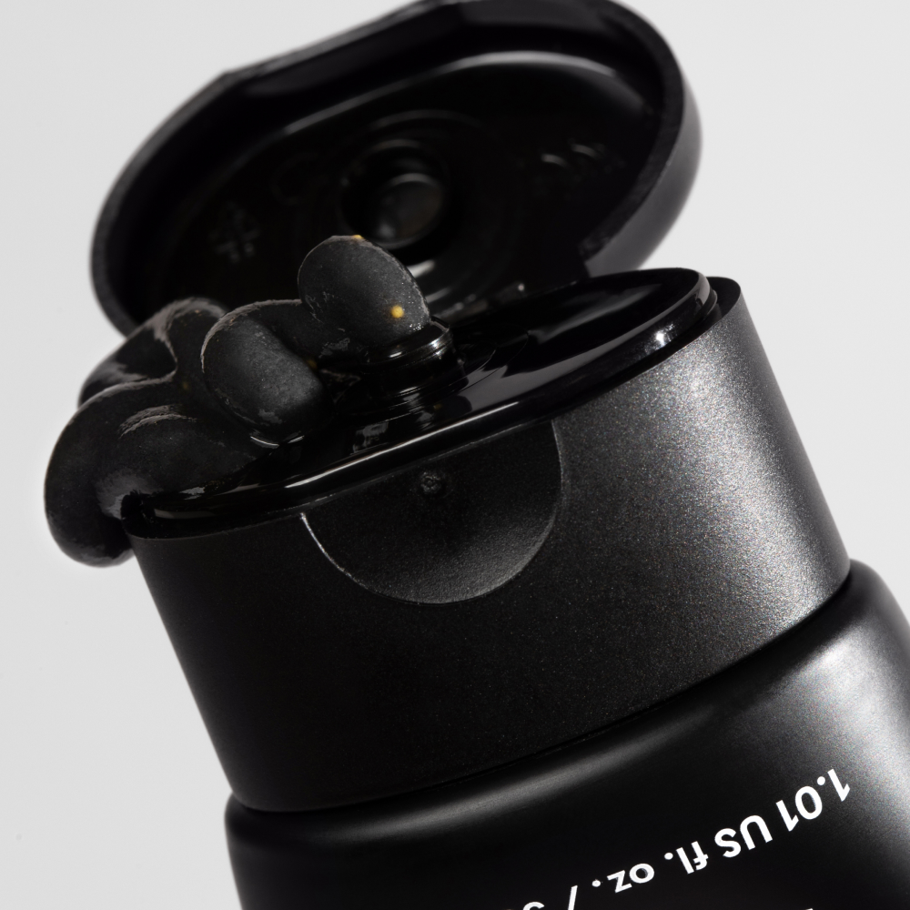Black skincare tube with flipped cap dispensing thick black charcoal facial mask cream.