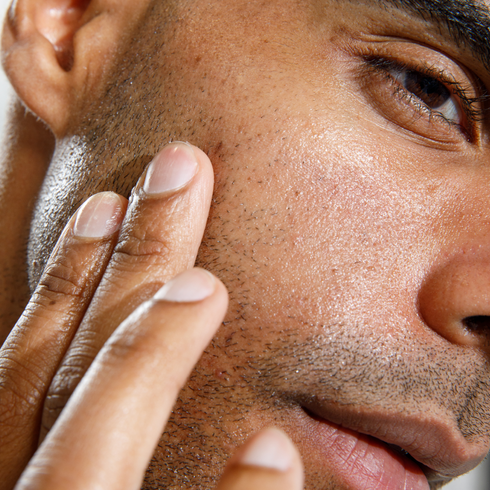 Close-up of man applying skincare cream on smooth, glowing dark skin with visible stubble and clear complexion.