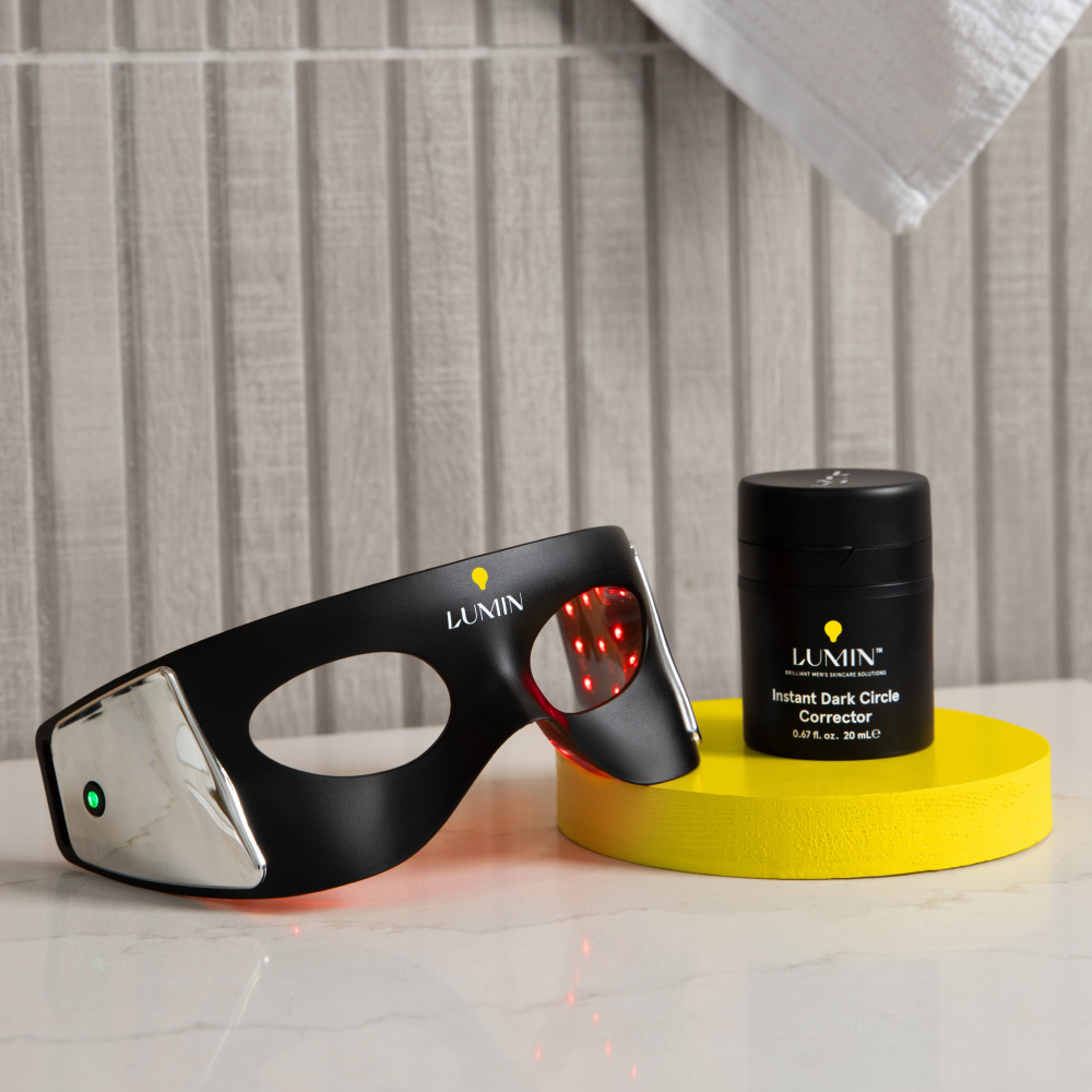 Lumin men's skincare LED eye mask with red light therapy and Instant Dark Circle Corrector cream on yellow platform