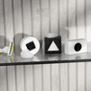 Razor and three black-and-white geometric soap bars with square, triangle, and circle shapes on glass shelf with foam bubbles.