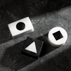Black and white geometric blocks with cutout shapes including circle, triangle, and square on textured dark surface.